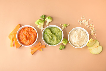 Bowls with healthy baby food on color background