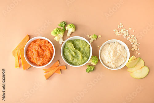 Bowls with healthy baby food on color background photo