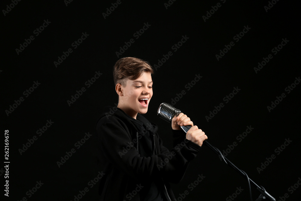 Teenage boy with microphone singing against dark background Teenage boy with microphone singing against dark background