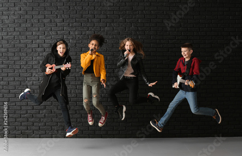 Φωτογραφία Jumping band of teenage musicians against dark wall