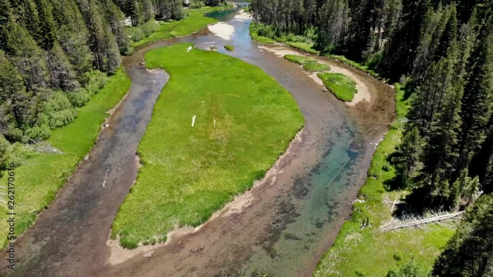 Drone panning shot of a flowing river with a surrounding forest mid day with bright colors and blue sky Drone panning shot of a flowing river with a surrounding forest mid day with bright colors and blue sky