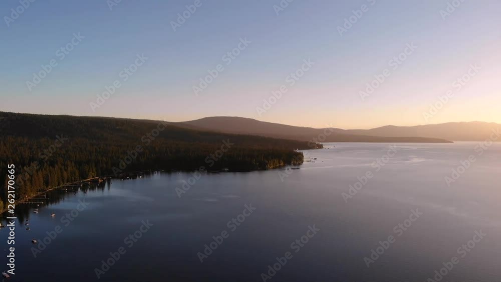 Drone shot sliding to the right while flying over a lake with a glowing sunset over the horizon. Drone shot sliding to the right while flying over a lake with a glowing sunset over the horizon.