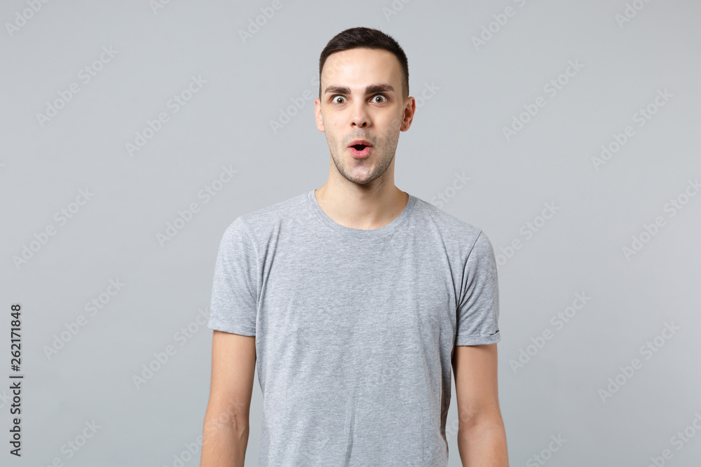 Portrait of amazed shocked young man in casual clothes keeping mouth open and looking camera isolated on grey wall background in studio. People sincere emotions, lifestyle concept. Mock up copy space. Portrait of amazed shocked young man in casual clothes keeping mouth open and looking camera isolated on grey wall background in studio. People sincere emotions, lifestyle concept. Mock up copy space.