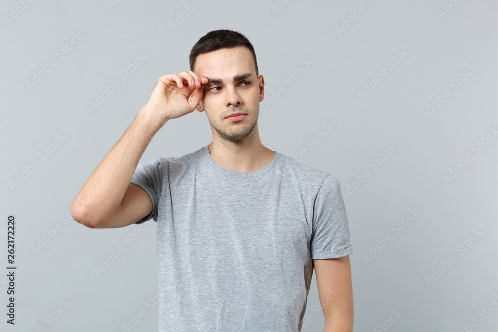Portrait of dissatisfied crying young man in casual clothes looking aside, keeping hand near eye isolated on grey background in studio. People sincere emotions, lifestyle concept. Mock up copy space. Portrait of dissatisfied crying young man in casual clothes looking aside, keeping hand near eye isolated on grey background in studio. People sincere emotions, lifestyle concept. Mock up copy space.
