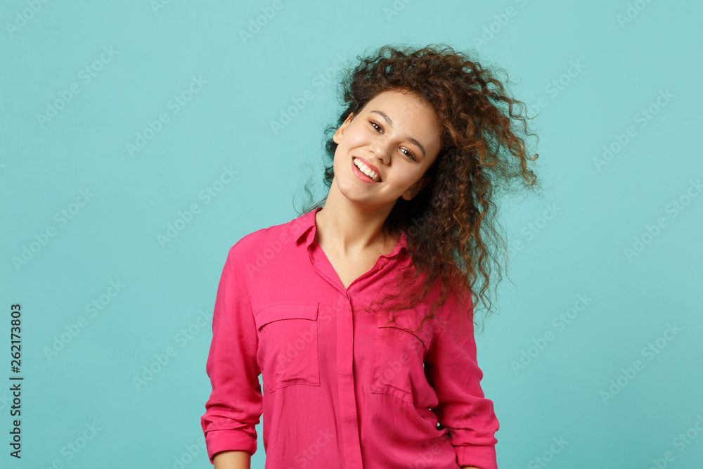 Fototapeta premium Portrait of attractive african girl in casual clothes standing with flowing hair isolated on blue turquoise wall background in studio. People sincere emotions, lifestyle concept. Mock up copy space.