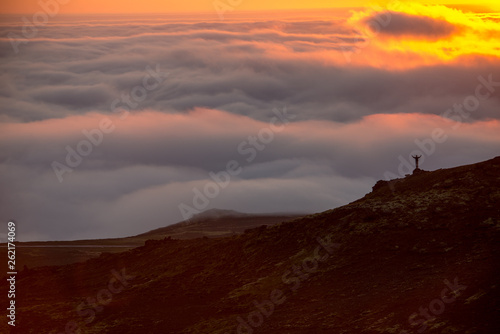 Silhouette of a man on the ridge above the sea of clouds, misty mountains at sunset in Iceland