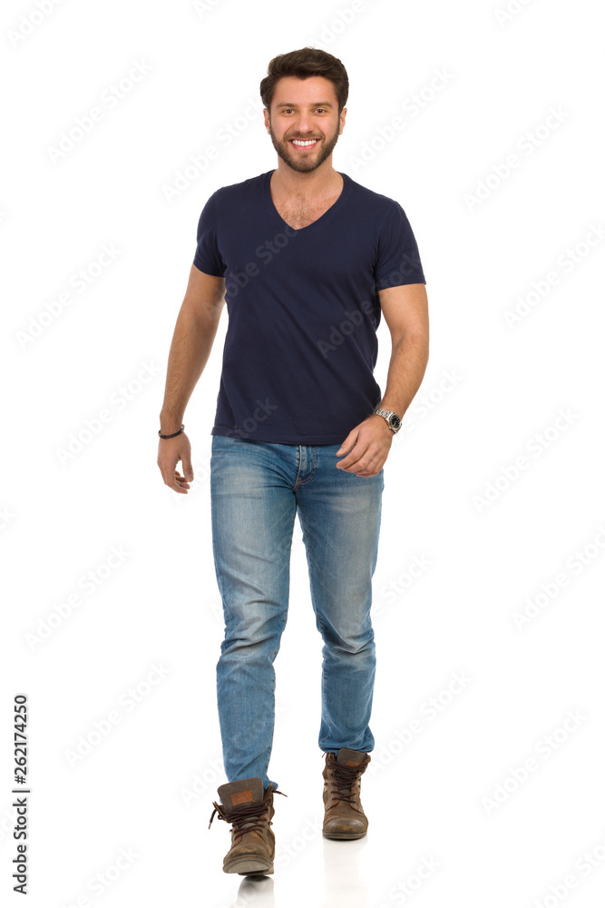 Smiling Man In Blue T-shirt, Jeans And Boots Is Walking Towards Camera Smiling Man In Blue T-shirt, Jeans And Boots Is Walking Towards Camera