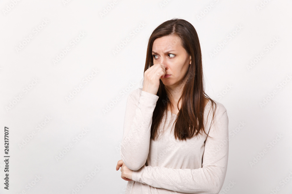 Portrait of disconcerted young woman in light clothes looking aside covering nose with hand isolated on white wall background in studio. People sincere emotions, lifestyle concept. Mock up copy space. Portrait of disconcerted young woman in light clothes looking aside covering nose with hand isolated on white wall background in studio. People sincere emotions, lifestyle concept. Mock up copy space.