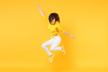 Cheerful funny young woman in summer casual clothes jumping and spreading hands isolated on yellow orange wall background in studio. People sincere emotions, lifestyle concept. Mock up copy space.