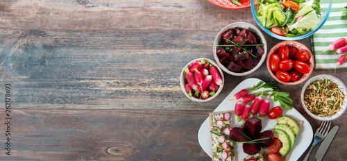 bowls and plate of healthy vegan salad . Various vegetables avocado, cucumber, radishes on wooden background