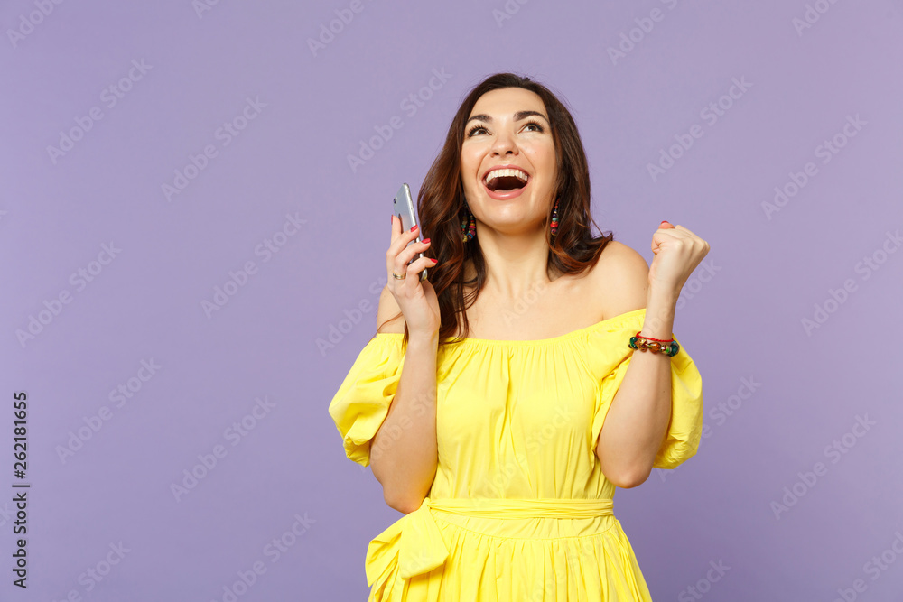 Happy young woman in summer dress using mobile phone, typing sms message, doing winner gesture, looking up isolated on violet background. People sincere emotions lifestyle concept. Mock up copy space. Happy young woman in summer dress using mobile phone, typing sms message, doing winner gesture, looking up isolated on violet background. People sincere emotions lifestyle concept. Mock up copy space.