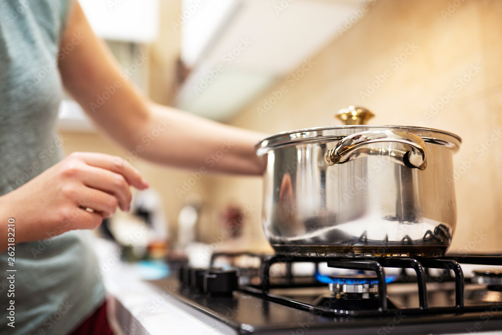 Beautiful young woman housewife prepairing dinner, hold in hands big steel saucepan, standing it on gas-stove. Beautiful young woman housewife prepairing dinner, hold in hands big steel saucepan, standing it on gas-stove.
