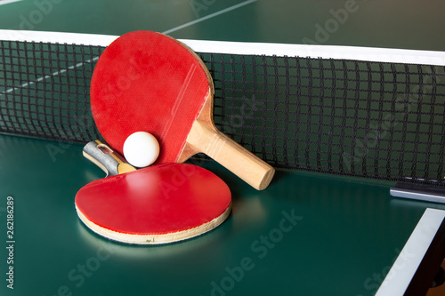 Two ping-pong rackets and a ball on a green table. ping-pong net.