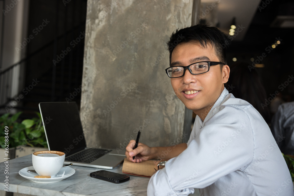 Side view of smiling Asian freelancer writing notes