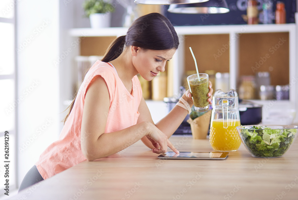 Beautiful young woman using a digital tablet in the kitchen Beautiful young woman using a digital tablet in the kitchen