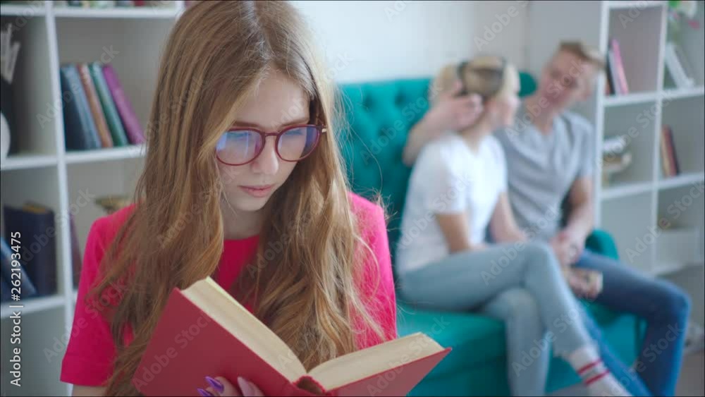 Female dork is reading tutorial while couple hugging on the couch at the library Female dork is reading tutorial while couple hugging on the couch at the library