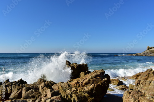 Wild waves breaking against the rocks. Blue sky, sunny day, Castro de Baroña, Galicia, Spain.