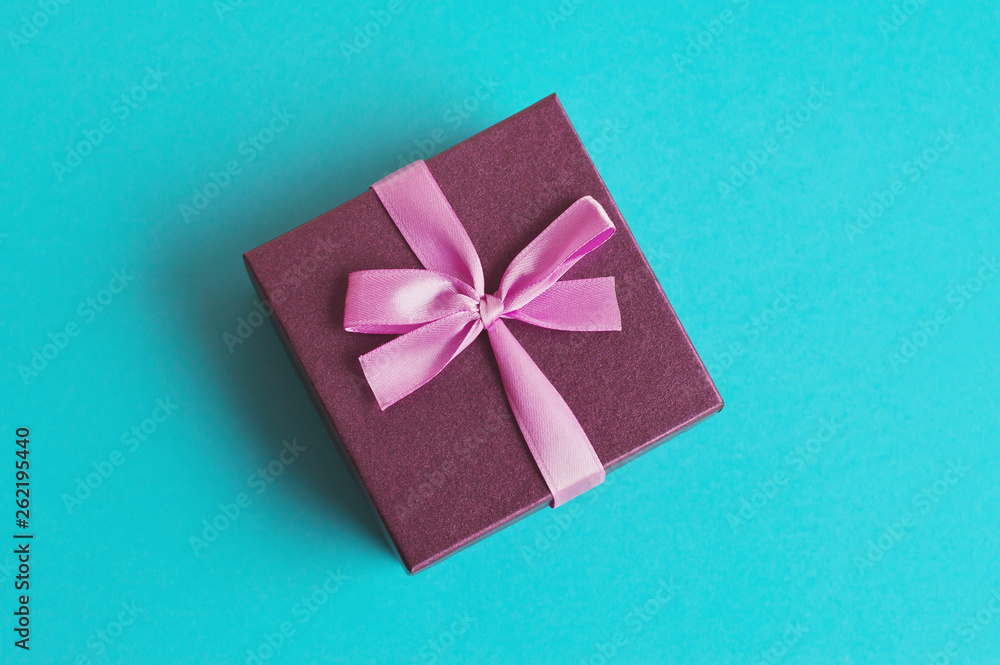 Small purple gift box with pink ribbon on turquoise background. Present for anniversary, birthday, New Year, Christmas Small purple gift box with pink ribbon on turquoise background. Present for anniversary, birthday, New Year, Christmas