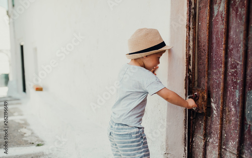 A small toddler boy with hat standing by a house in town on summer holiday. © Halfpoint