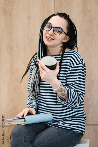 young  smiling dreadlock girl in black glasses making notes in her notebook