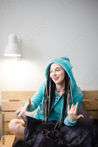 portrait of young woman with dreadlocks in cute jacket with ears sitting on the bed 