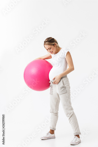 Beautiful young pregnant yoga fitness woman posing isolated over white wall background make exercises with ball. © Drobot Dean