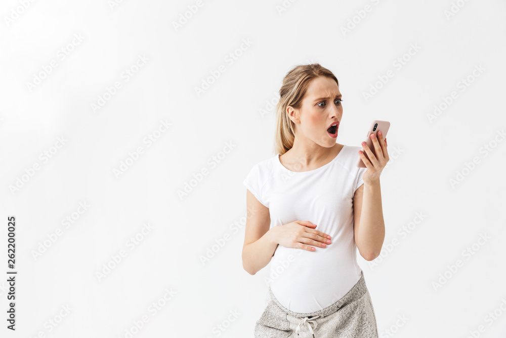 Displeased young pregnant woman posing isolated over white wall background talking by phone.