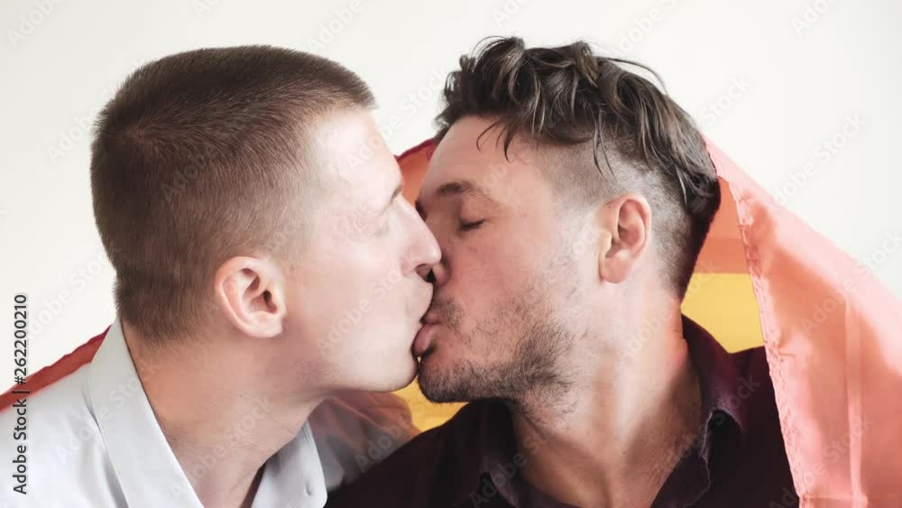 Young gay male couple passionately kiss with pride rainbow flag. Close up. Happy gay friendship, relationship, pride concept. Young gay male couple passionately kiss with pride rainbow flag. Close up. Happy gay friendship, relationship, pride concept.