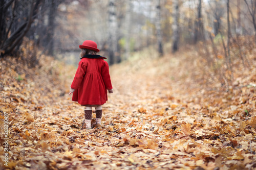 Child girl in red coat and hat walks autumn forest