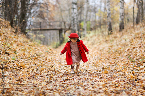 Child girl in red coat and hat walks autumn forest