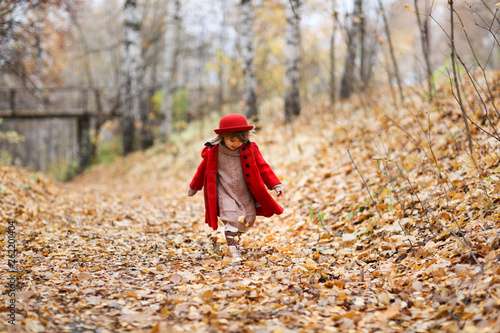 Child girl in red coat and hat walks autumn forest