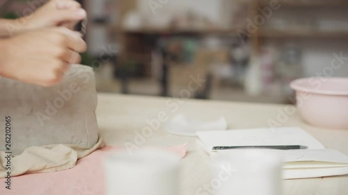 Tracking left close-up of unrecognizable female ceramic artist cutting piece of clay with string photo