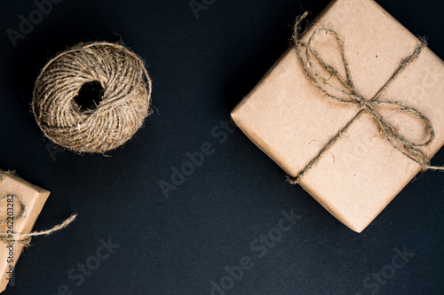 Handcrafted gift box wrapped in Craft paper with rope and bow on black background. Top view, flat lay.