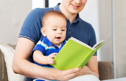 family, parenthood and people concept - happy father and little baby son with book at home
