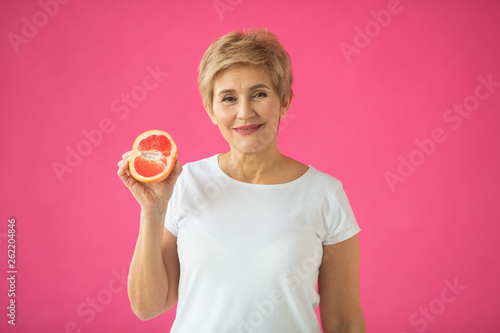 beautiful elderly woman in white T-shirt with grapefruits in her hands on a pink background