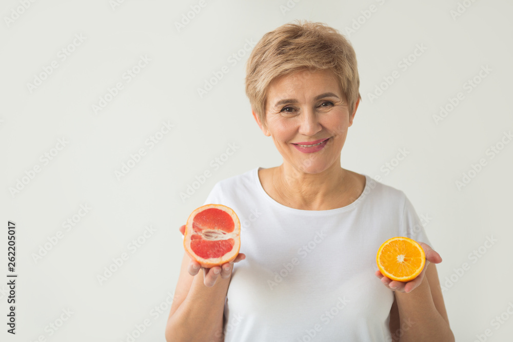 beautiful elderly woman in white t-shirt with orange and grape-fruit in hands on white background