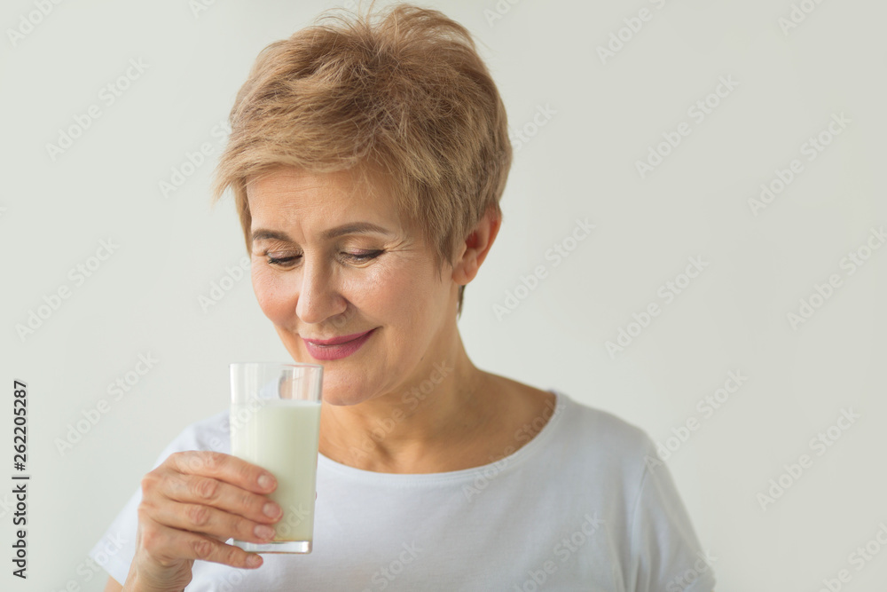 beautiful elderly woman in white T-shirt with a glass of milk on a white background beautiful elderly woman in white T-shirt with a glass of milk on a white background