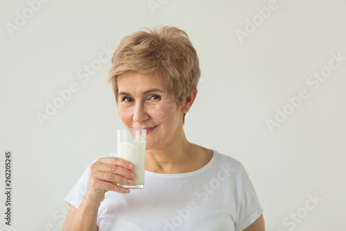 beautiful elderly woman in white T-shirt with a glass of milk on a white background