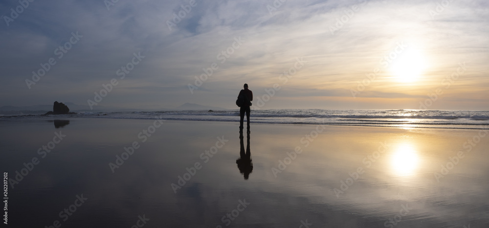Happy man with backpack, silhouette on the beach at sunset, Biarritz, France