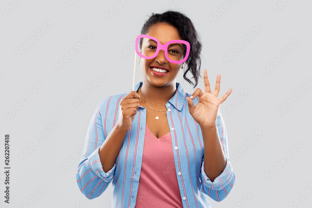 party props, photo booth and people concept - happy african american young woman with big glasses showing ok hand sign over grey background