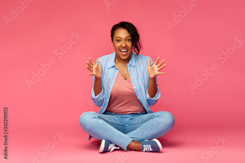 emotions, expressions and people concept - happy excited african american woman sitting on floor over pink background