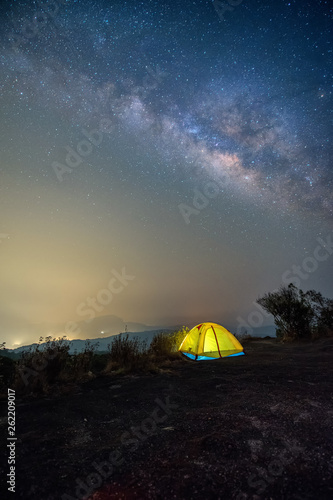A yellow tent in the dark night background is the milky way and many stars on the sky.