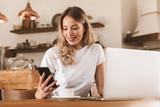 Portrait of attractive blond woman working on laptop and drinking coffee while sitting in cozy cafe indoor