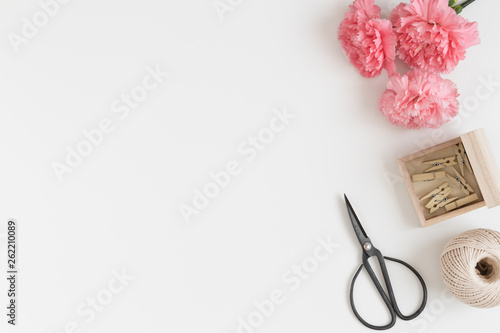 Workspace accessories and a bouquet of pink carnations on a white table.  Flat lay with blank copy space.