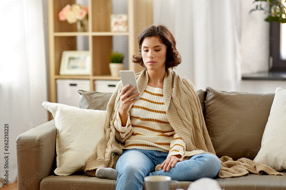 Obraz premium technology, health and cold concept - sad sick woman in blanket using smartphone at home