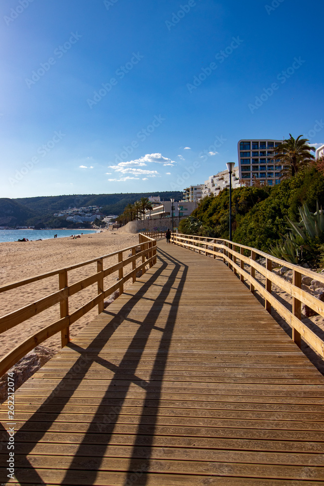 wooden walkway on the beach with the village of Sesimbra in the background