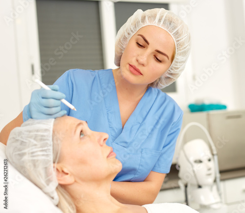 Plastic surgeon preparing for operation on mature woman face