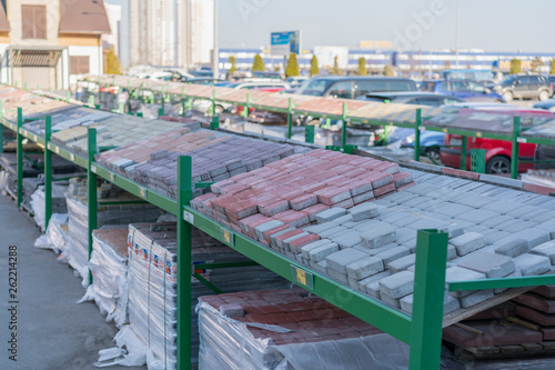 Store building materials and street tiles. Display of decorative paving stones and road bricks at a stoneyard shop organized on display pallets for sale stored on wooden shelves outdoors © jollier_