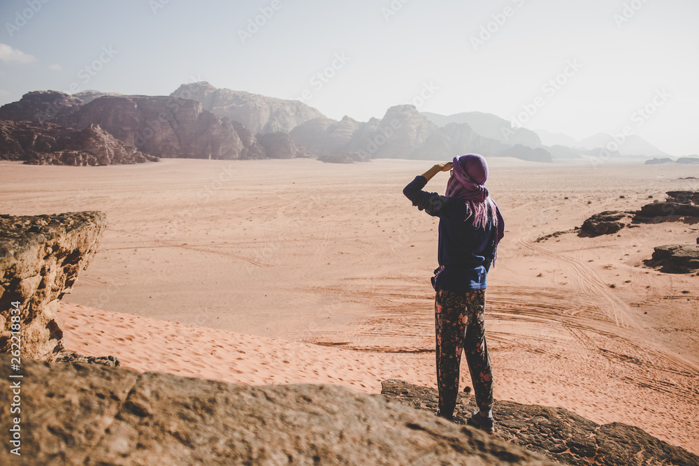 travel woman stay back to camera and looking from below hand near face on a dramatic Wadi Rum Jordanian desert world famous heritage touristic place scenic landscape location, mountain background