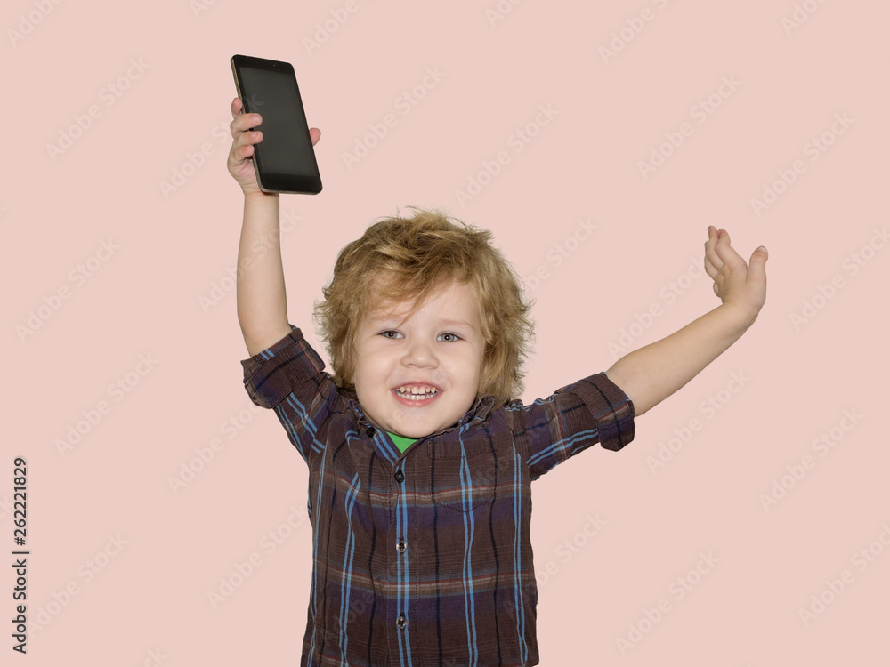 A little toddler boy picks up a smartphone gadget above his head. A satisfied child is happy that he was allowed to play phones with his smartphone. A little toddler boy picks up a smartphone gadget above his head. A satisfied child is happy that he was allowed to play phones with his smartphone.